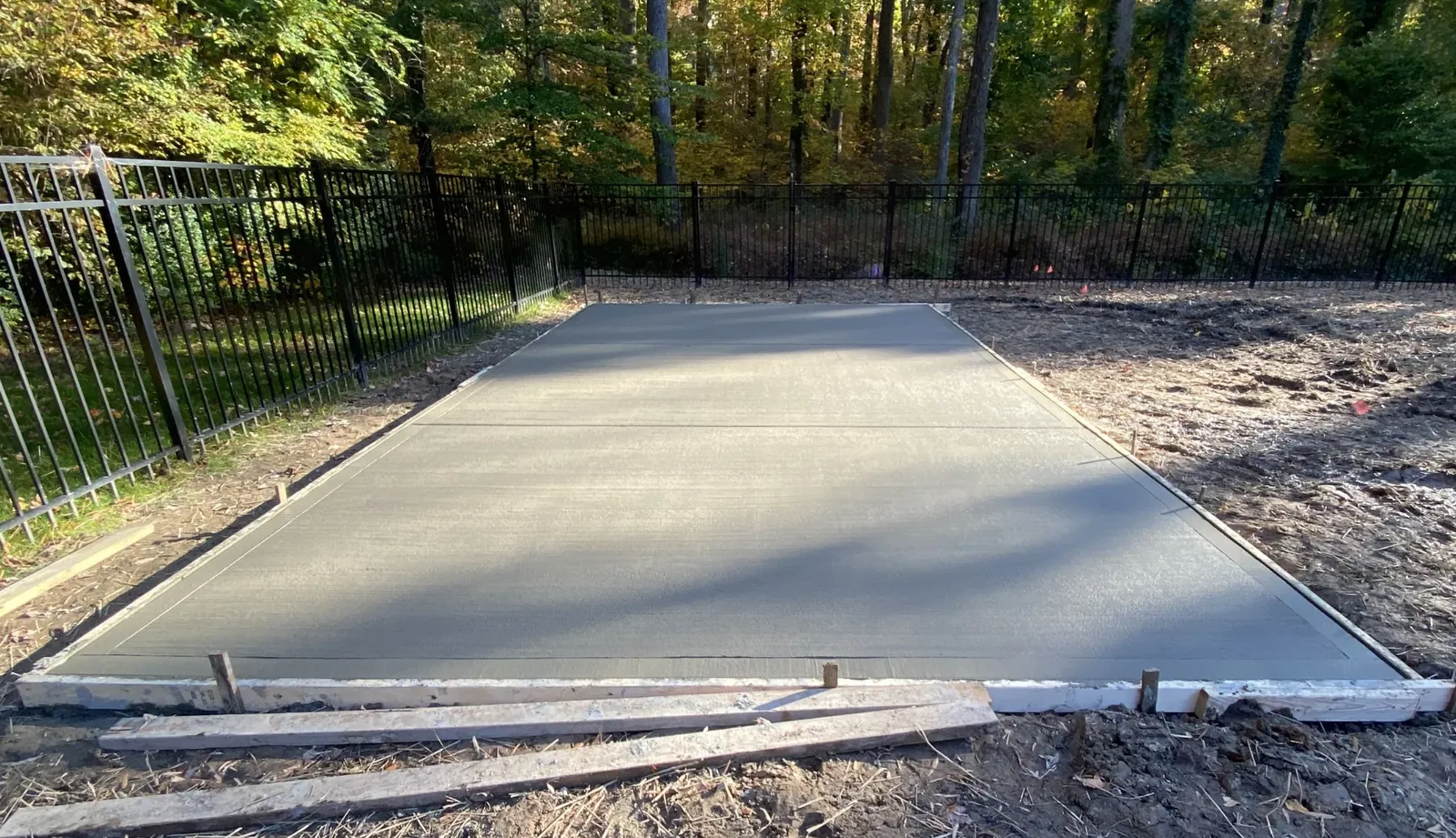 A finished concrete parking pad with cut control joints in a fenced back lot — Little Acres Grading
