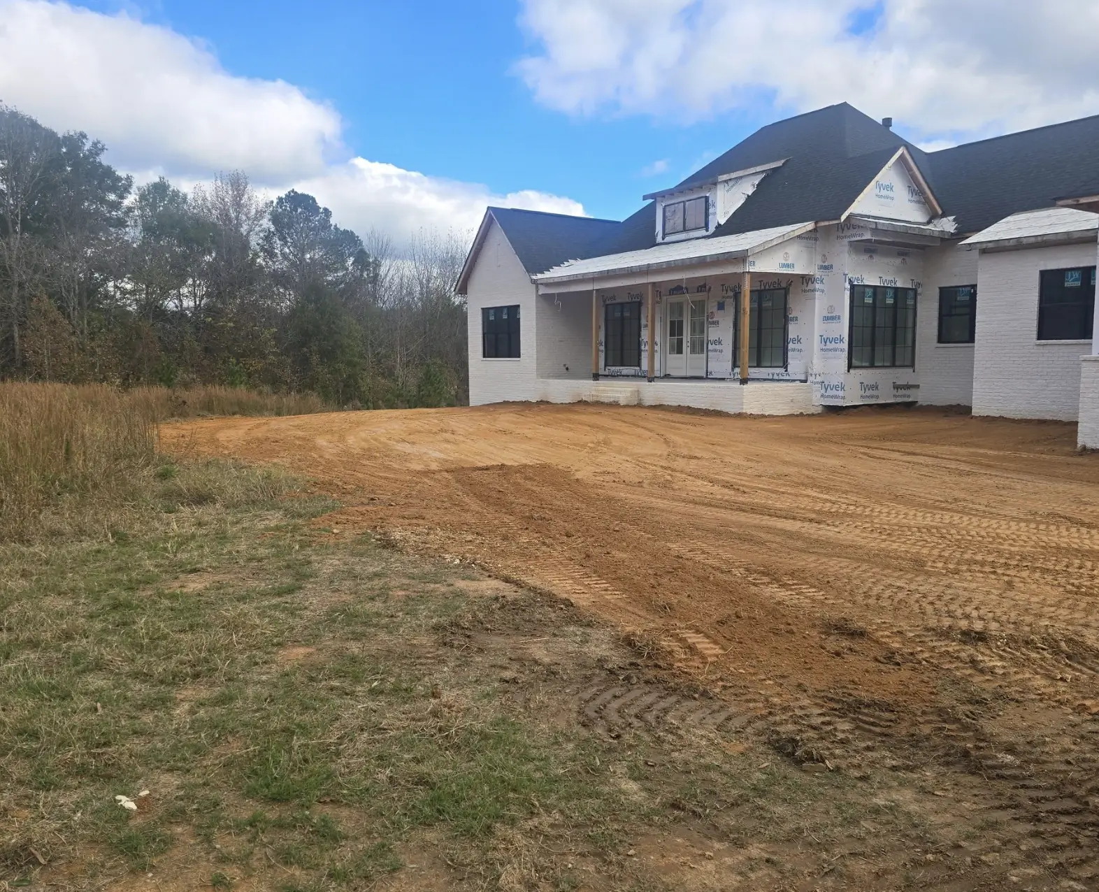 A red-clay yard cut to grade around a white farmhouse under construction — Little Acres Grading