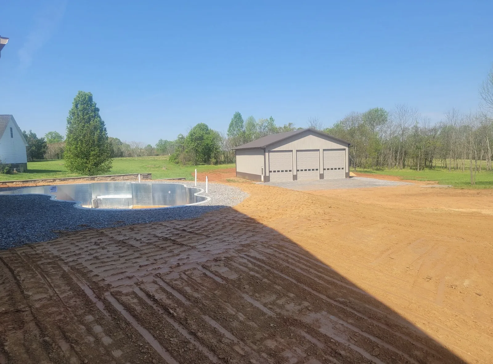 A graded yard and stone pool surround beside a newly built shop building — Little Acres Grading