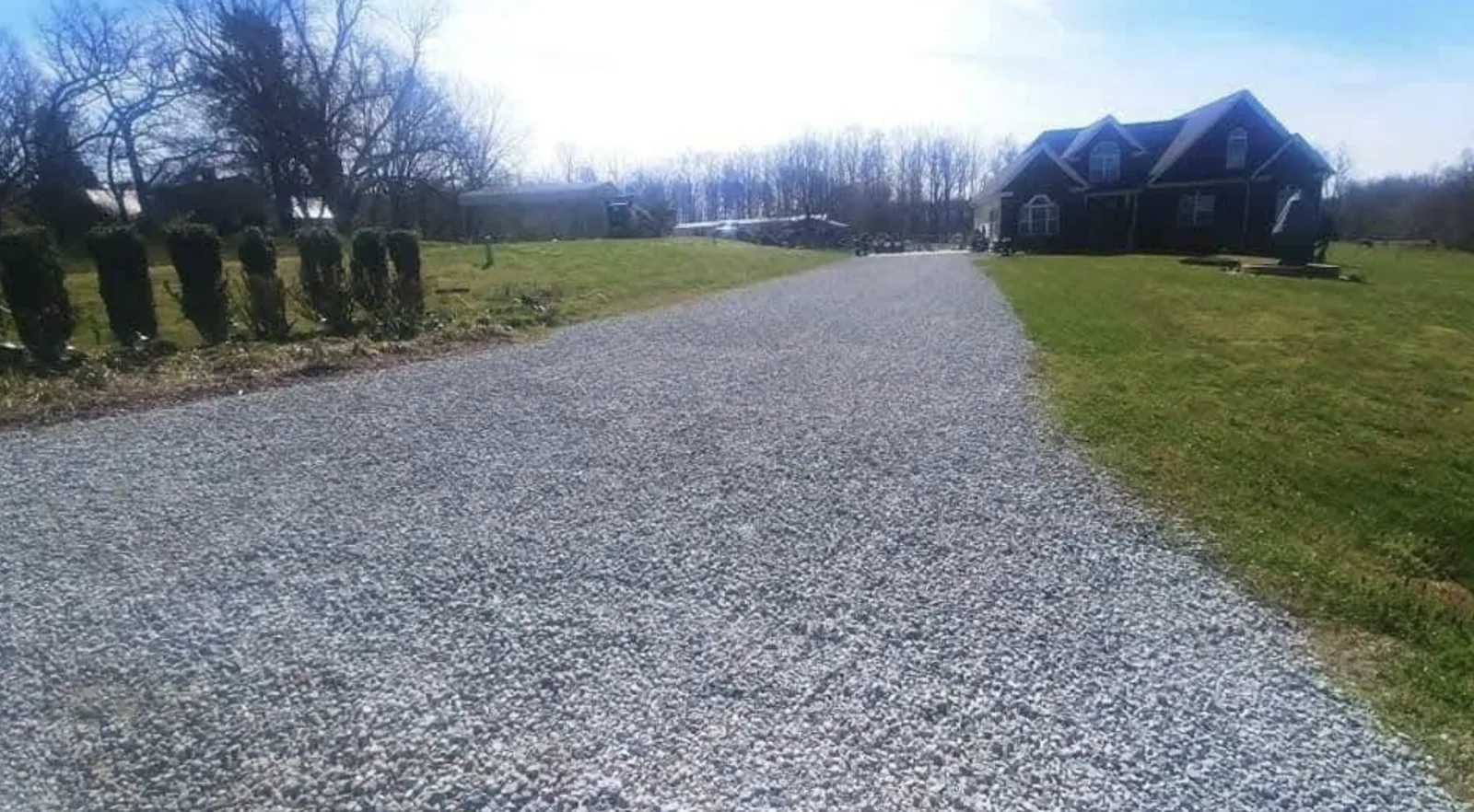 A wide gravel driveway running up to a stone-front home in winter — Little Acres Grading
