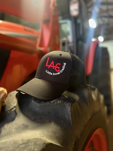A Little Acres Grading cap resting on a tractor tyre in the yard at Cherryville