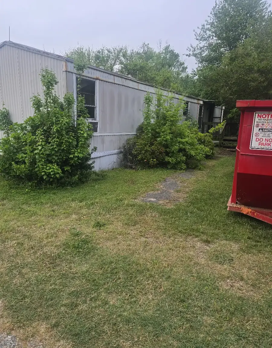 An abandoned mobile home grown over with brush before demolition — Little Acres Grading