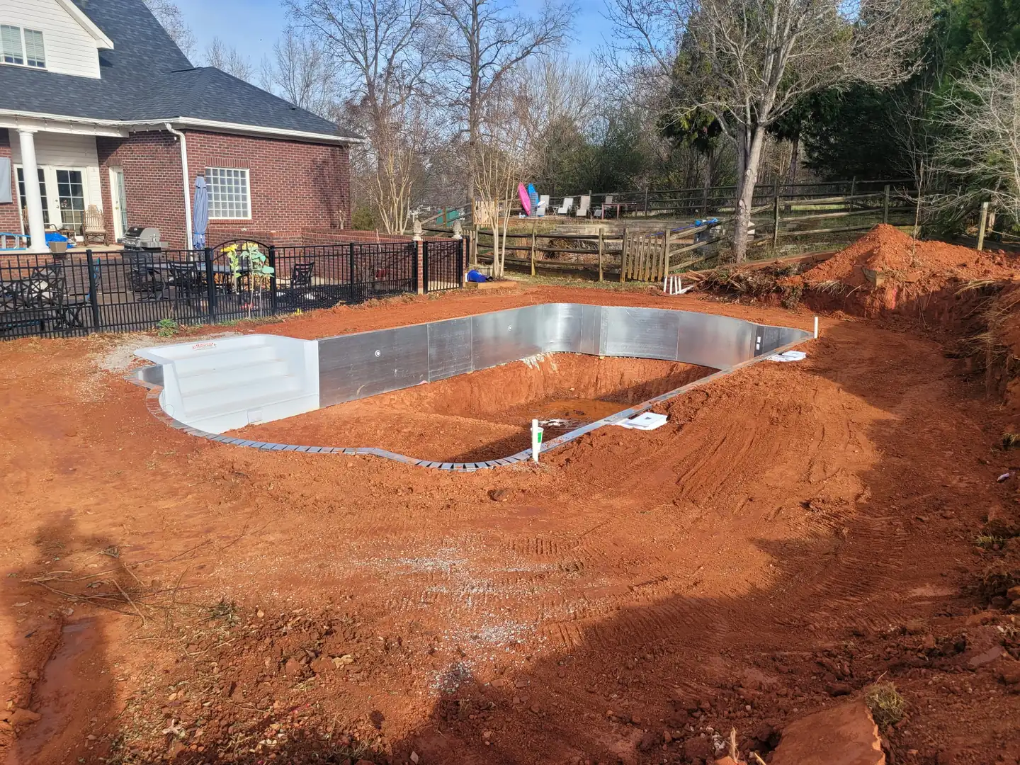 A pool dug and walled in behind a brick home with the spoil graded off — Little Acres Grading