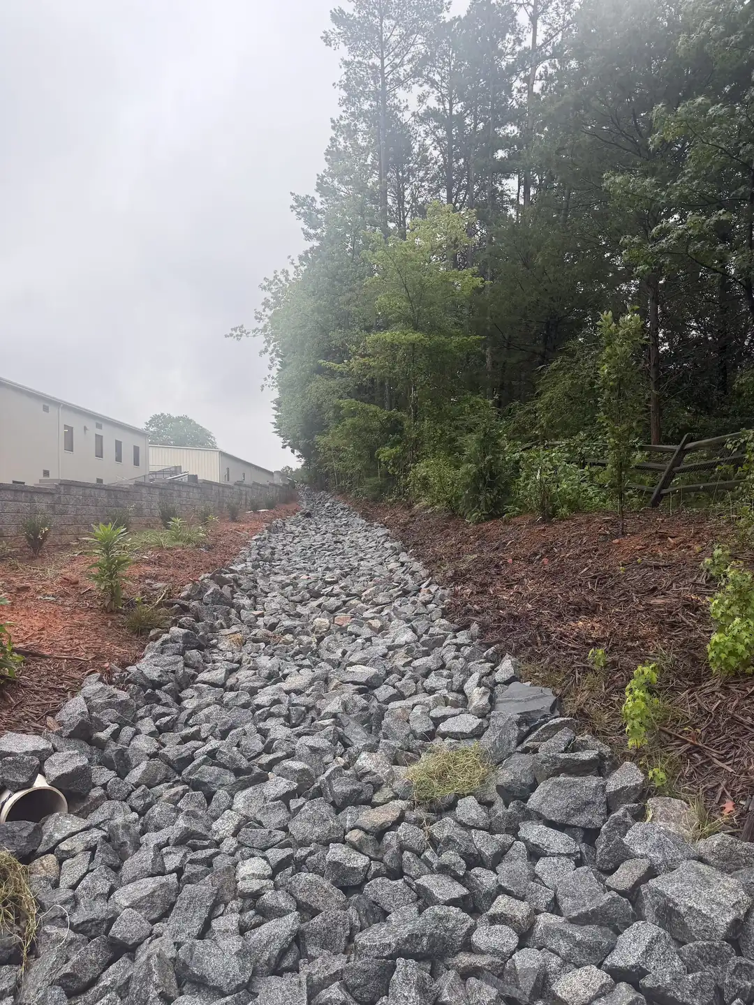 A rip-rap drainage channel cut behind a commercial building — Little Acres Grading