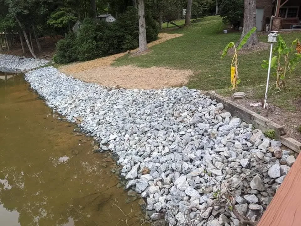 A lake bank stabilized with graded rip-rap above the waterline — Little Acres Grading