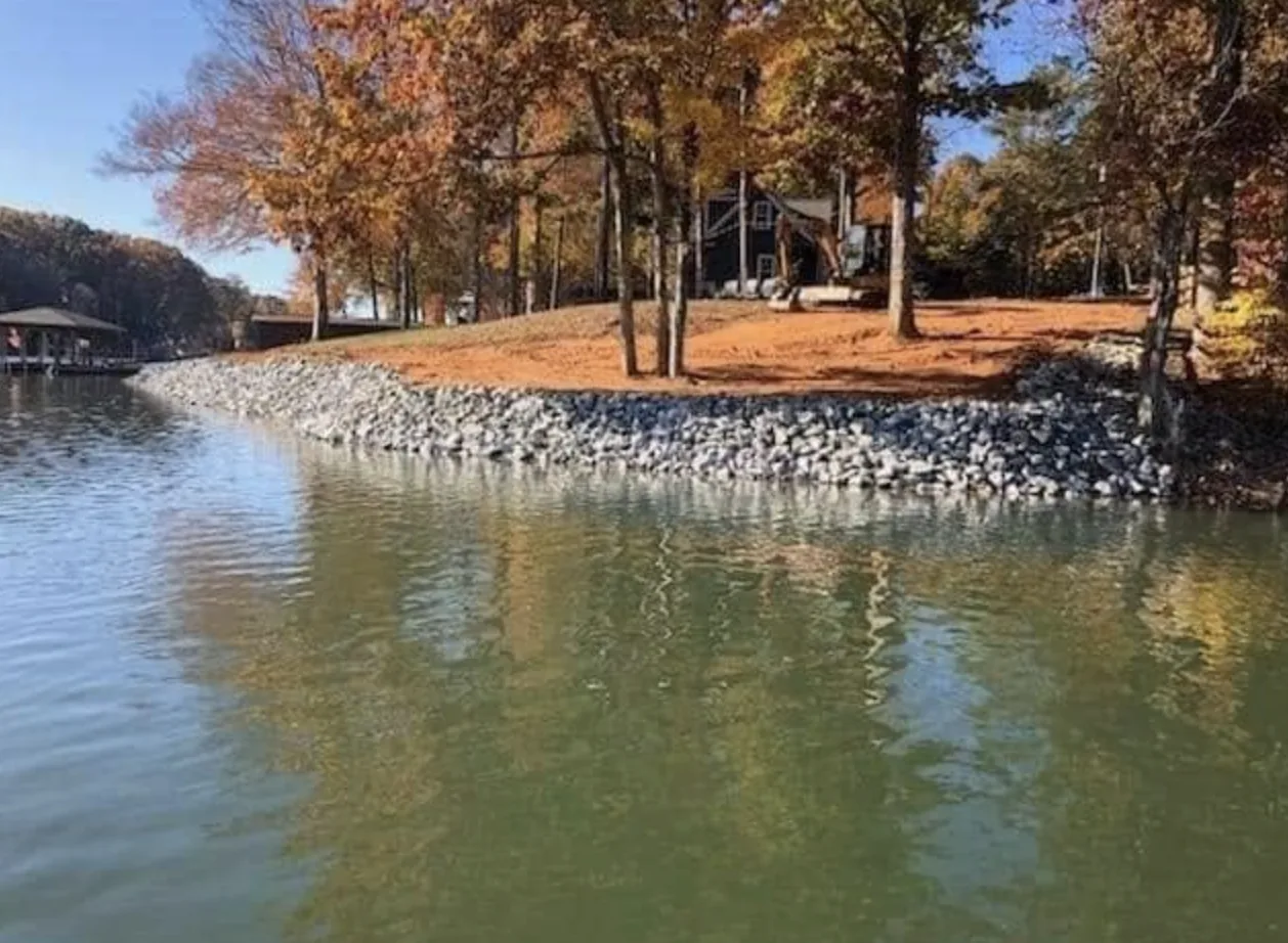 Rip-rap along a lake shoreline below a house in autumn colour — Little Acres Grading
