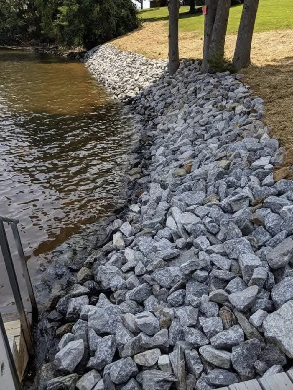 Rip-rap set tight along a lake shoreline beside a dock — Little Acres Grading