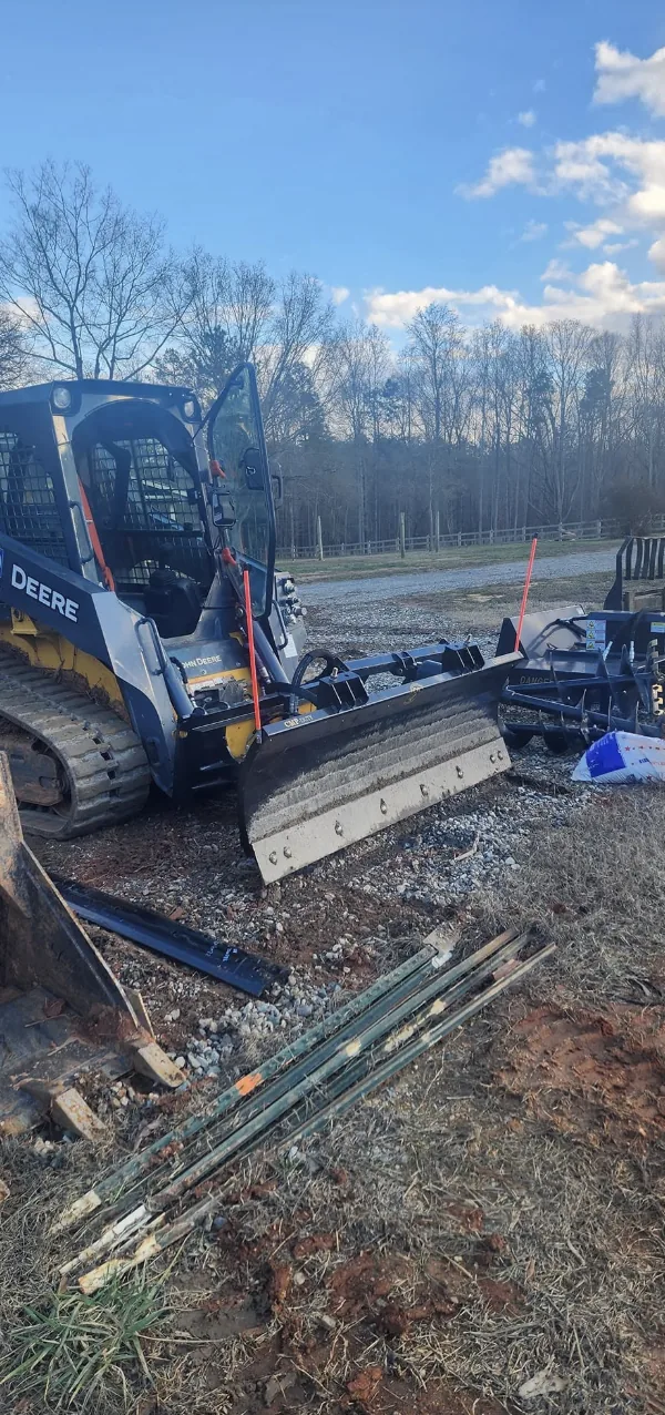 A skid steer fitted with a grading blade on a winter job site — Little Acres Grading